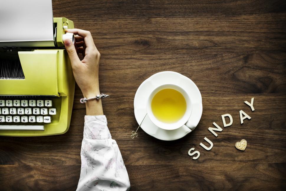 Free Image of Overhead view of a hand rotating a a typewriter s platen knob and a cup of lemon tea 