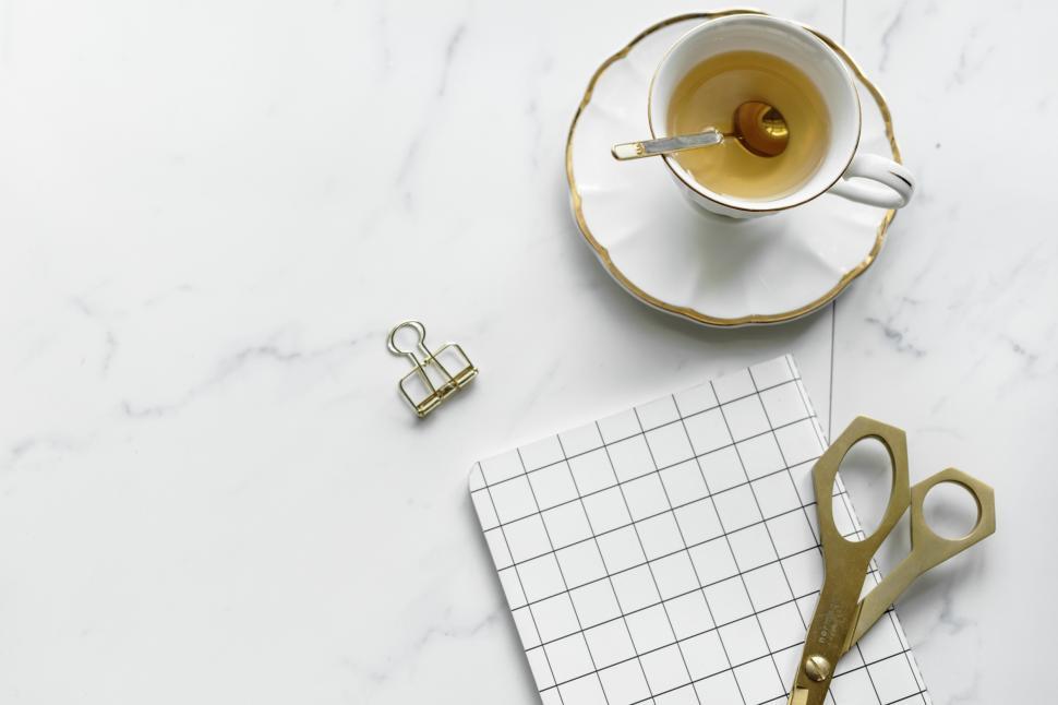 Free Image of Overhead view of scissors on a notebook surrounded with a cup of tea and a paperclip 