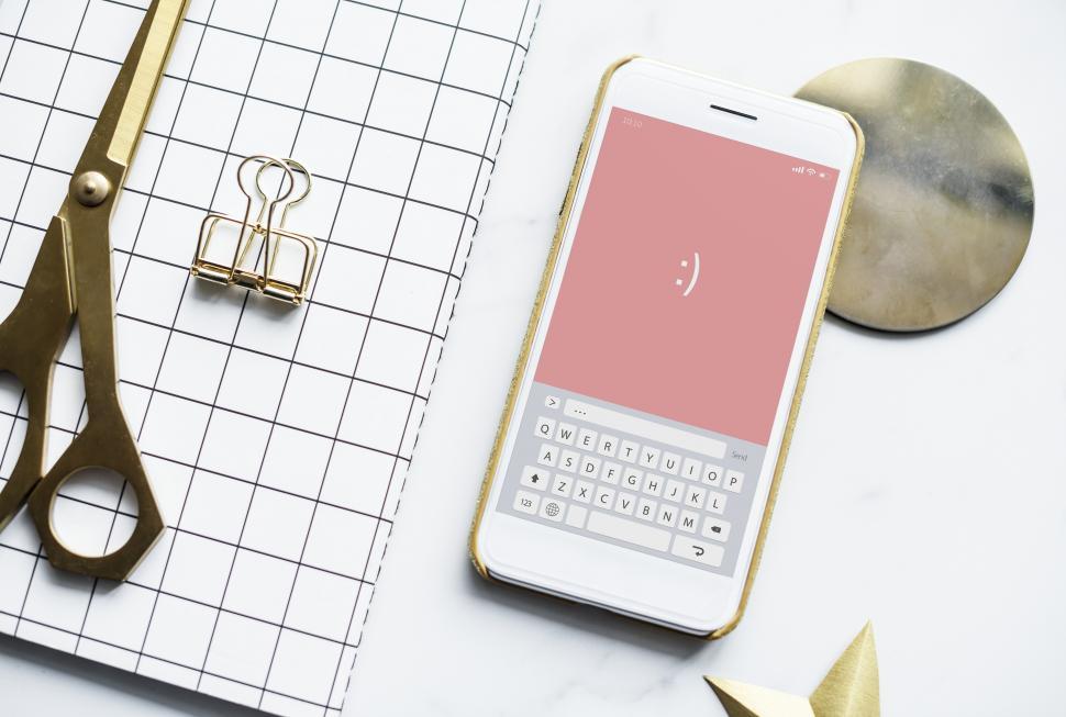 Free Image of Flat lay of a mobile phone with emoticon alongside a notebook and scissors 