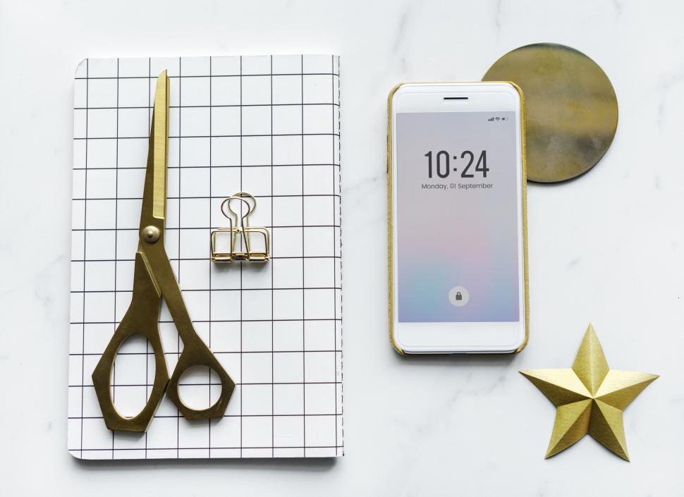 Free Image of Flat lay of a mobile phone showing the time alongside a notebook and scissors 