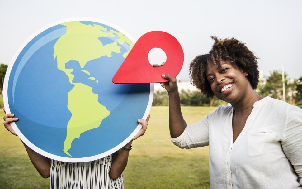Free Image of Two women holding a card board globe and location pin shaped cutouts 