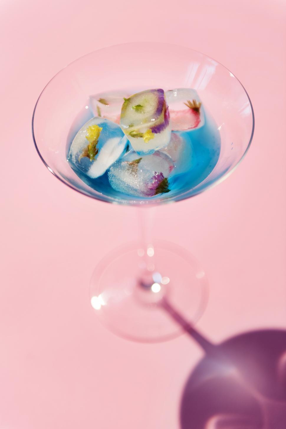 Free Image of Edible flower ice cubes in a martini glass, on pink background 