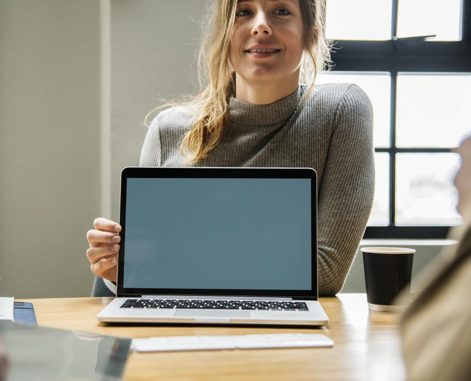 Free Image of A young smiling woman pointing at a laptop - blank screen 