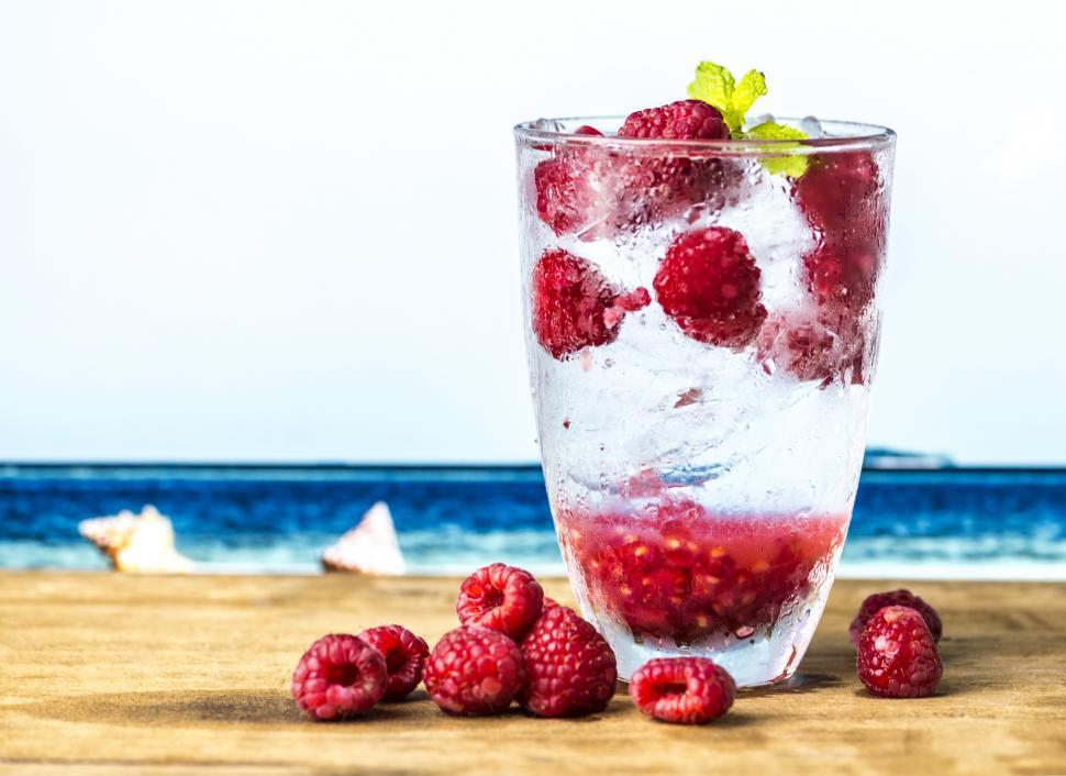 Free Image of Close up of a clear glass of beverage garnished with raspberries 