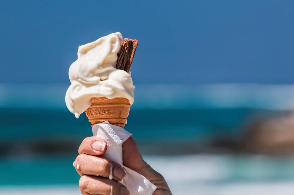 Free Image of Hand Holding Ice Cream Cone on Beach 