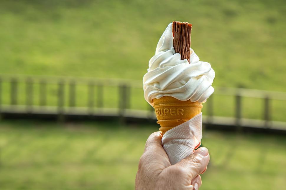 Free Image of Hand Holding Ice Cream Cone in Front of Green Field 
