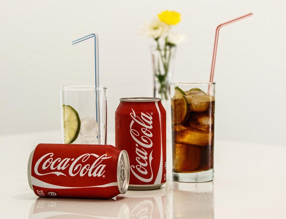 Free Image of Two Cans of Coca Cola Next to a Glass of Lemonade 