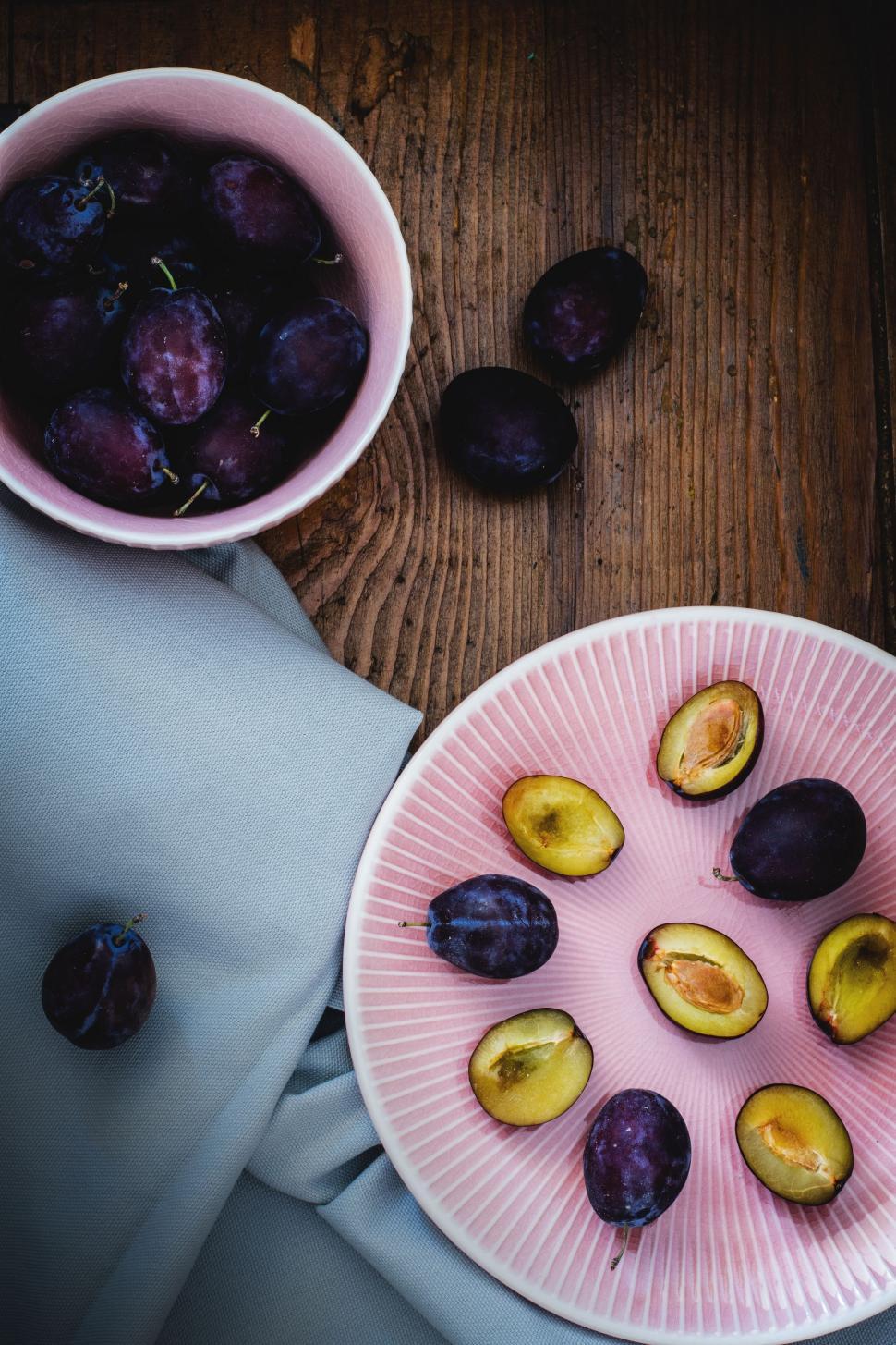 Free Image of Bowl and plate full of plums on grey table cloth  