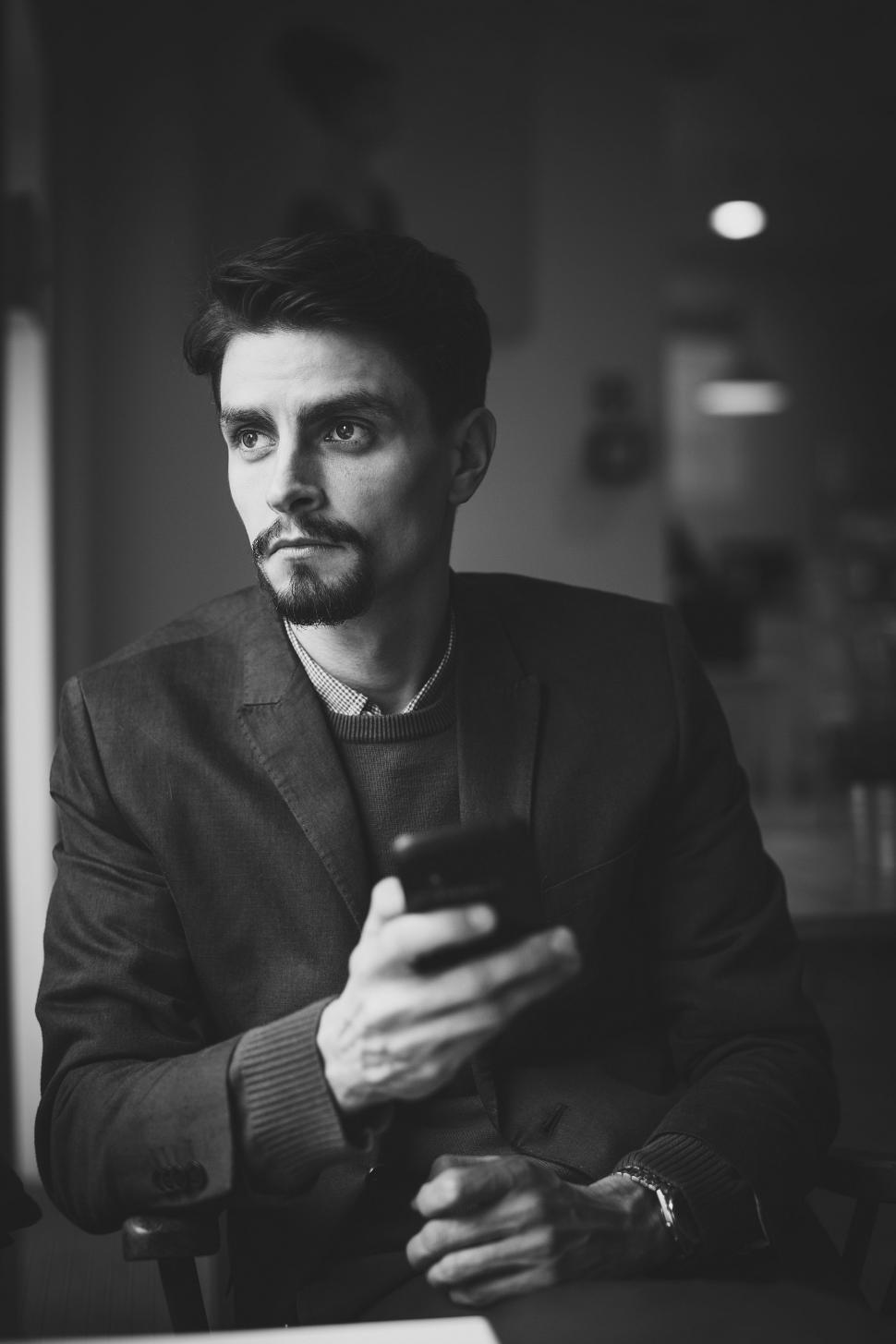 Free Image of Indoor View of young Man sitting and holding smartphone while looking away  