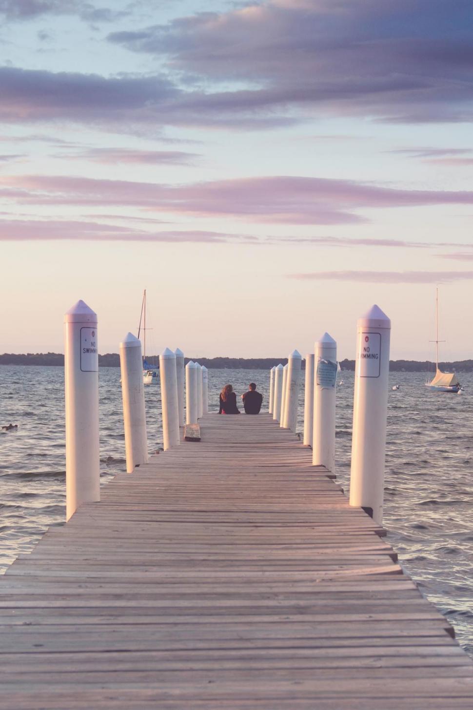 Free Image of Long View of Pier with Couple and sailboat  