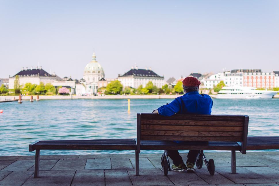 Free Image of Old man on bench enjoying lake and city view  