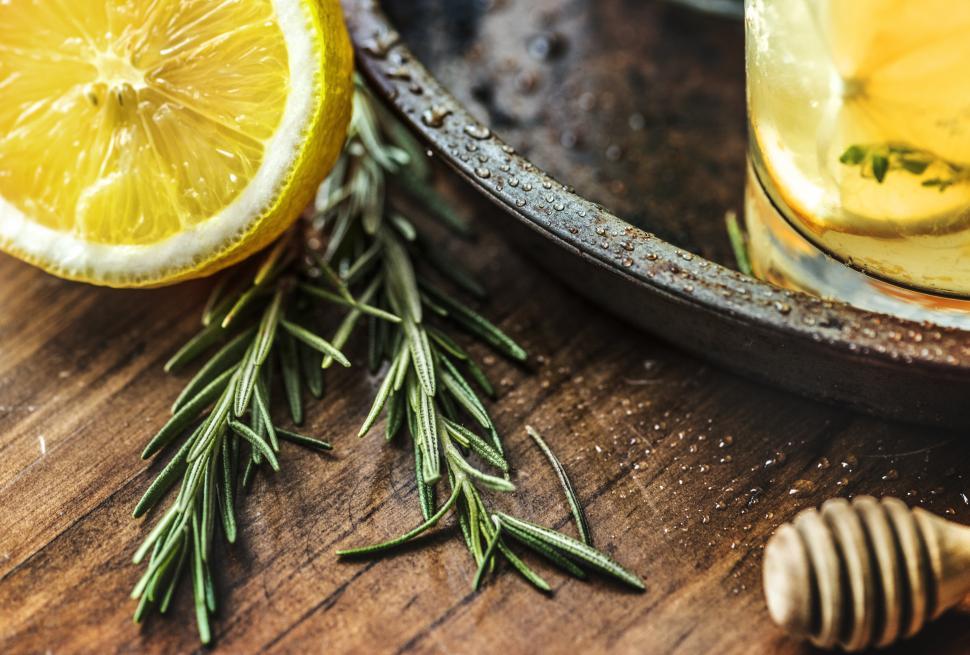 Free Image of Close up of a lemon cut in half, rosemary leaves and a honey dripper 