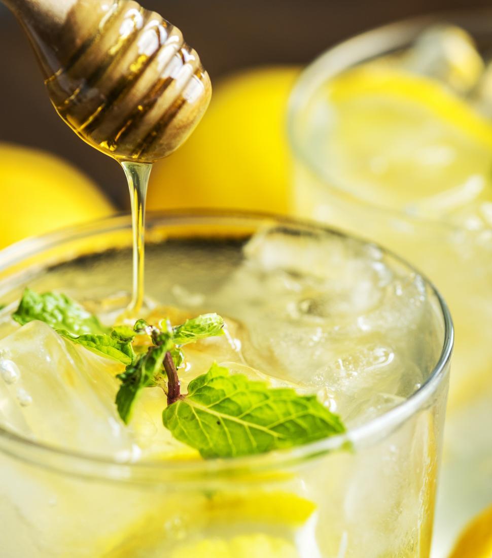 Free Image of Close up of honey being poured chilled beverage in a glass garnished with lemon slices 