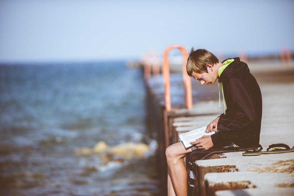 Free Image of Boy Reading Near Ocean  