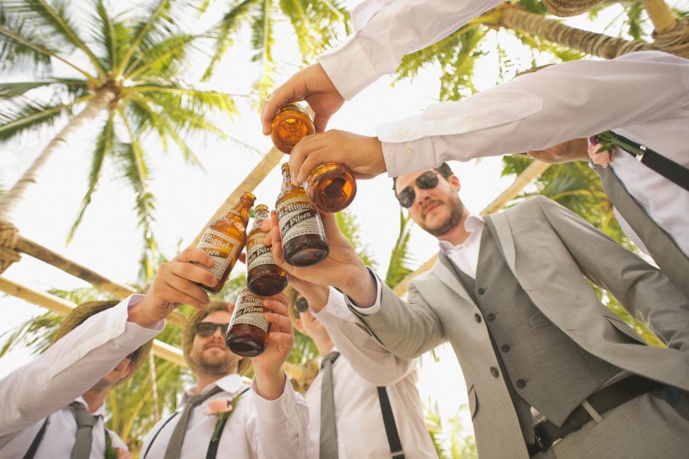 Free Image of Group of male friends clinking beer bottles at wedding 