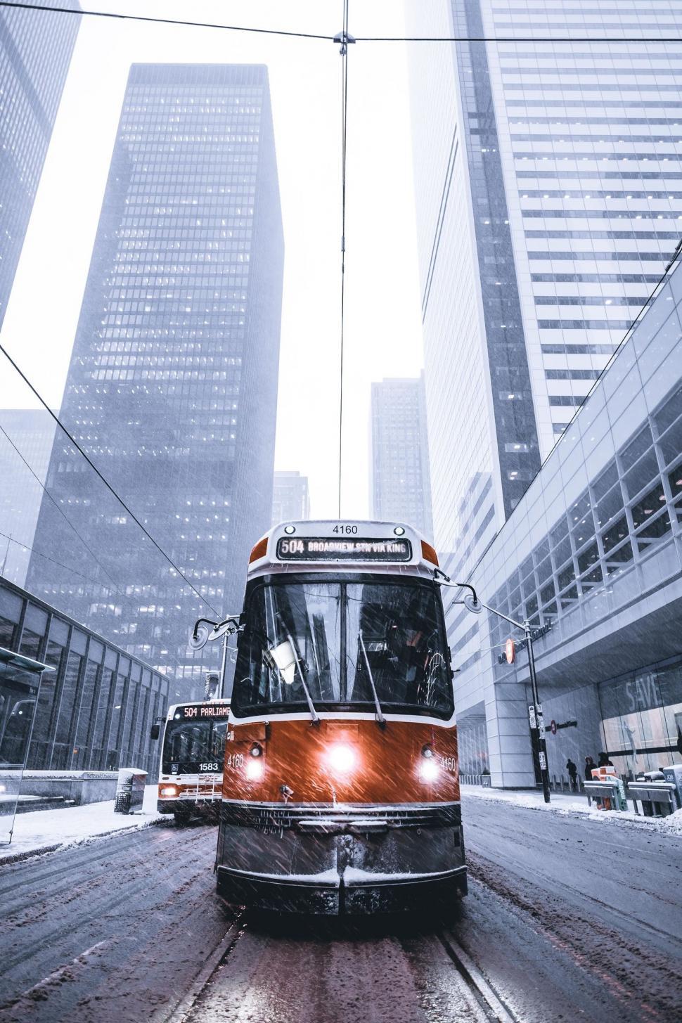 Free Image of Low Angle view of Tram on road with Skyscrapers in snowfall 