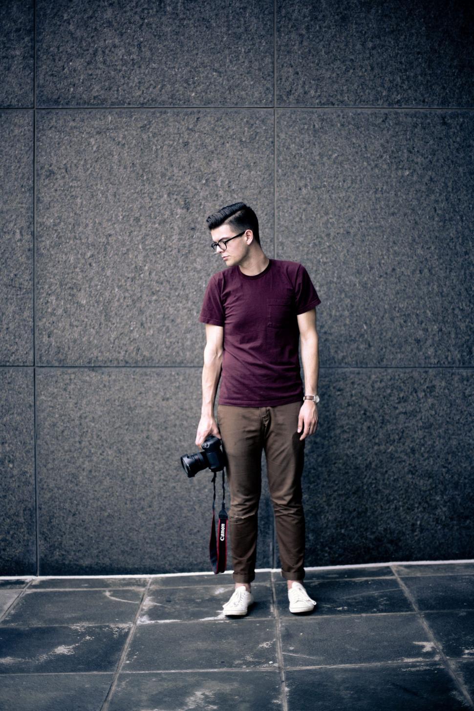 Free Image of Young Male Photographer Standing against wall on the pavement  