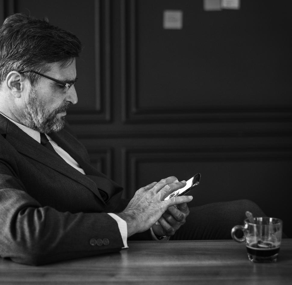 Free Image of Black and white of a bearded businessman looking at his mobile phone 