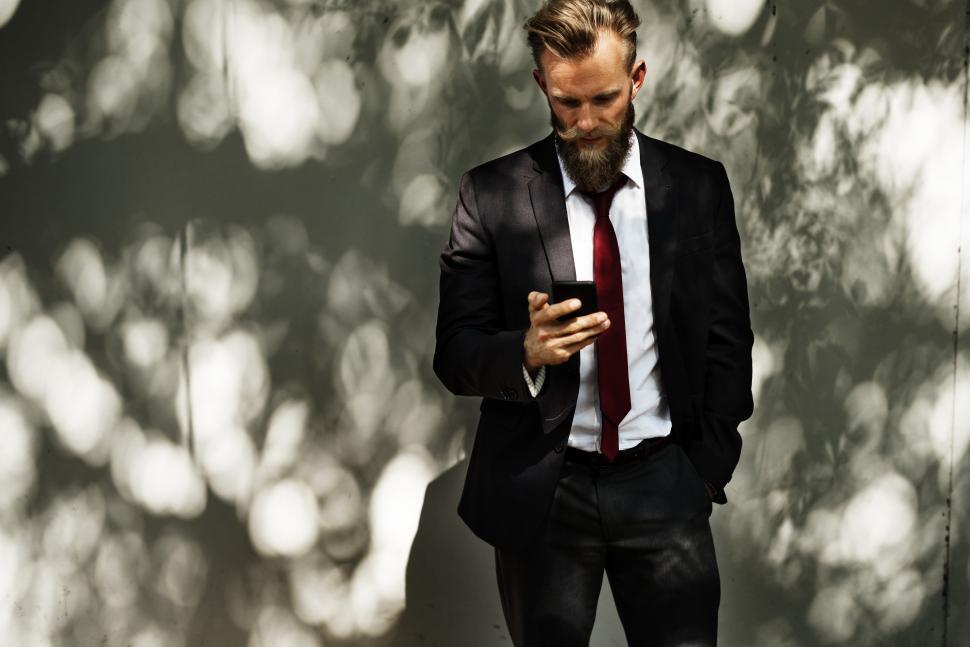 Free Image of A bearded man outdoors looking at his mobile phone 
