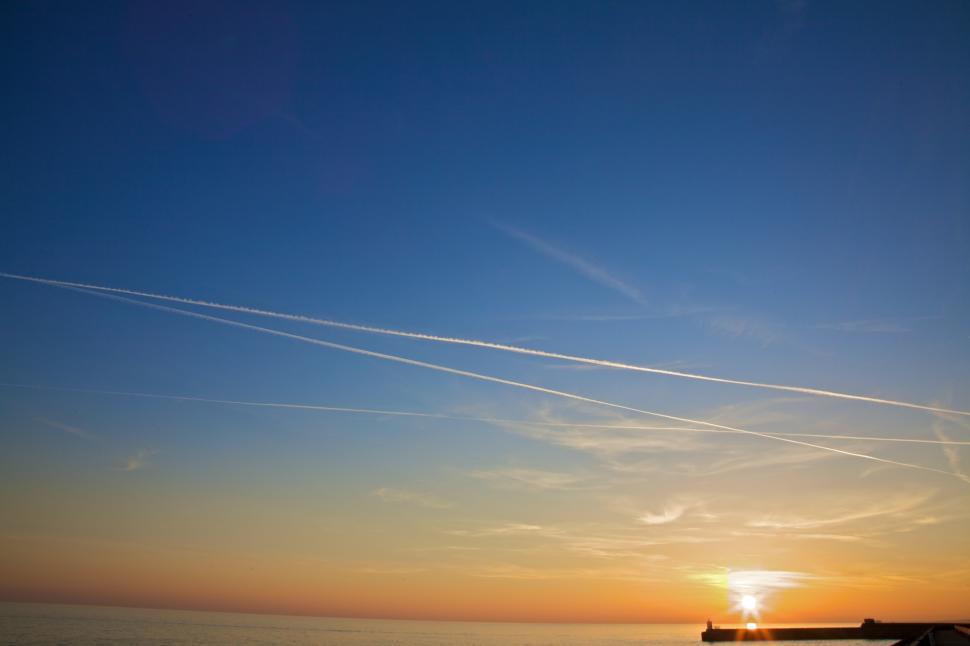 Free Image of Sun Setting Over Ocean With Contrails in Sky 
