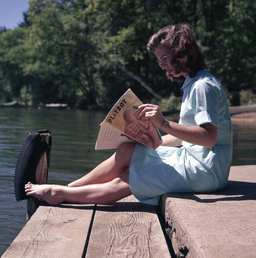 Free Image of Woman reading magazine on wooden pier  