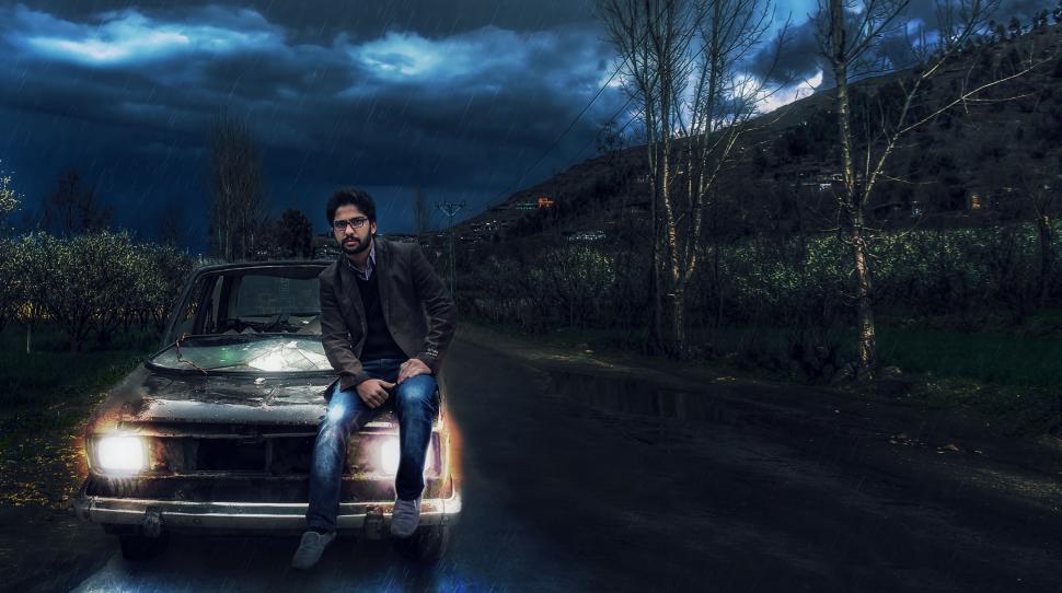 Free Image of Man Sitting on Car with Dramatic Dark Clouds 