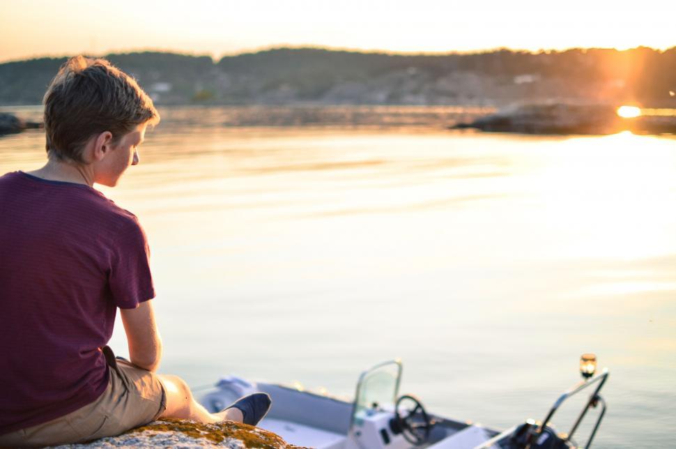 Free Image of Young Boy Sitting By Sea during sunset 