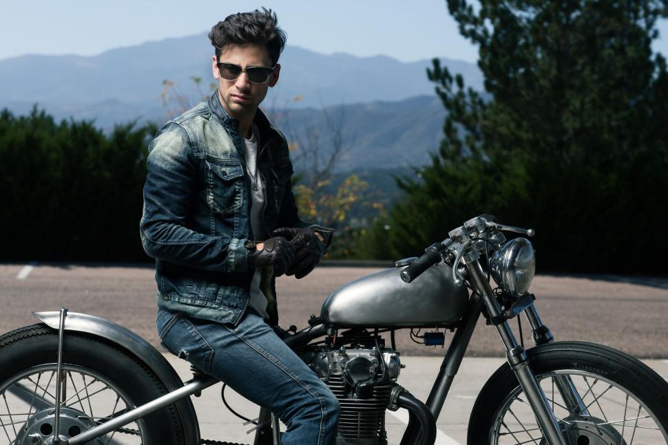 Free Image of Male Fashion Model Posing on Motorbike with mountains in the background  