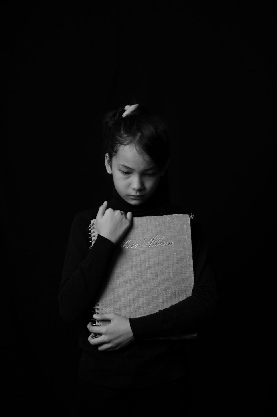 Free Image of Girl Child Hugging Photo Album on Black Background 