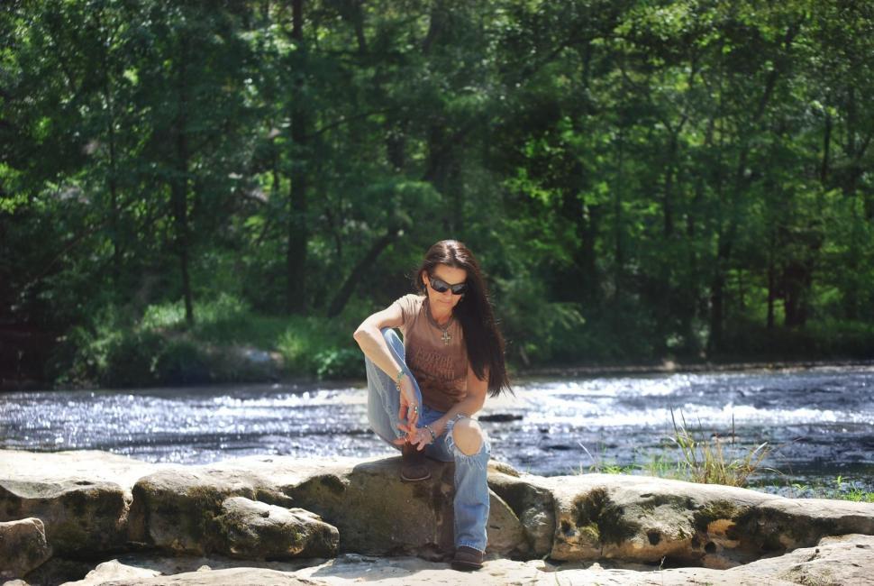 Free Image of Woman sitting on rock with trees and river - looking down  