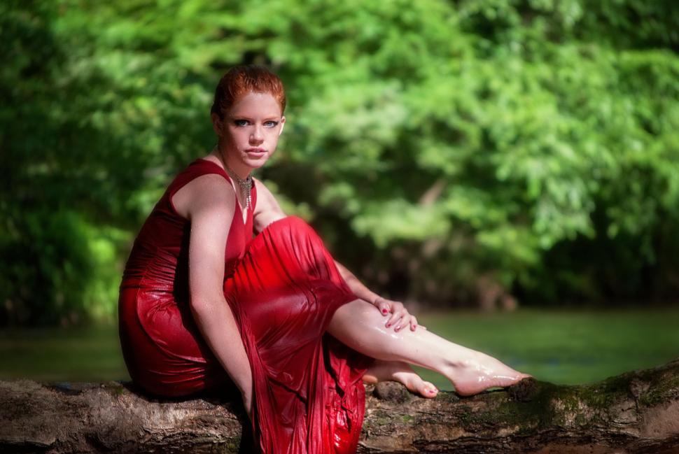 Free Image of Young Female Fashion Model in Wet Red Dress With Trees and Lake  