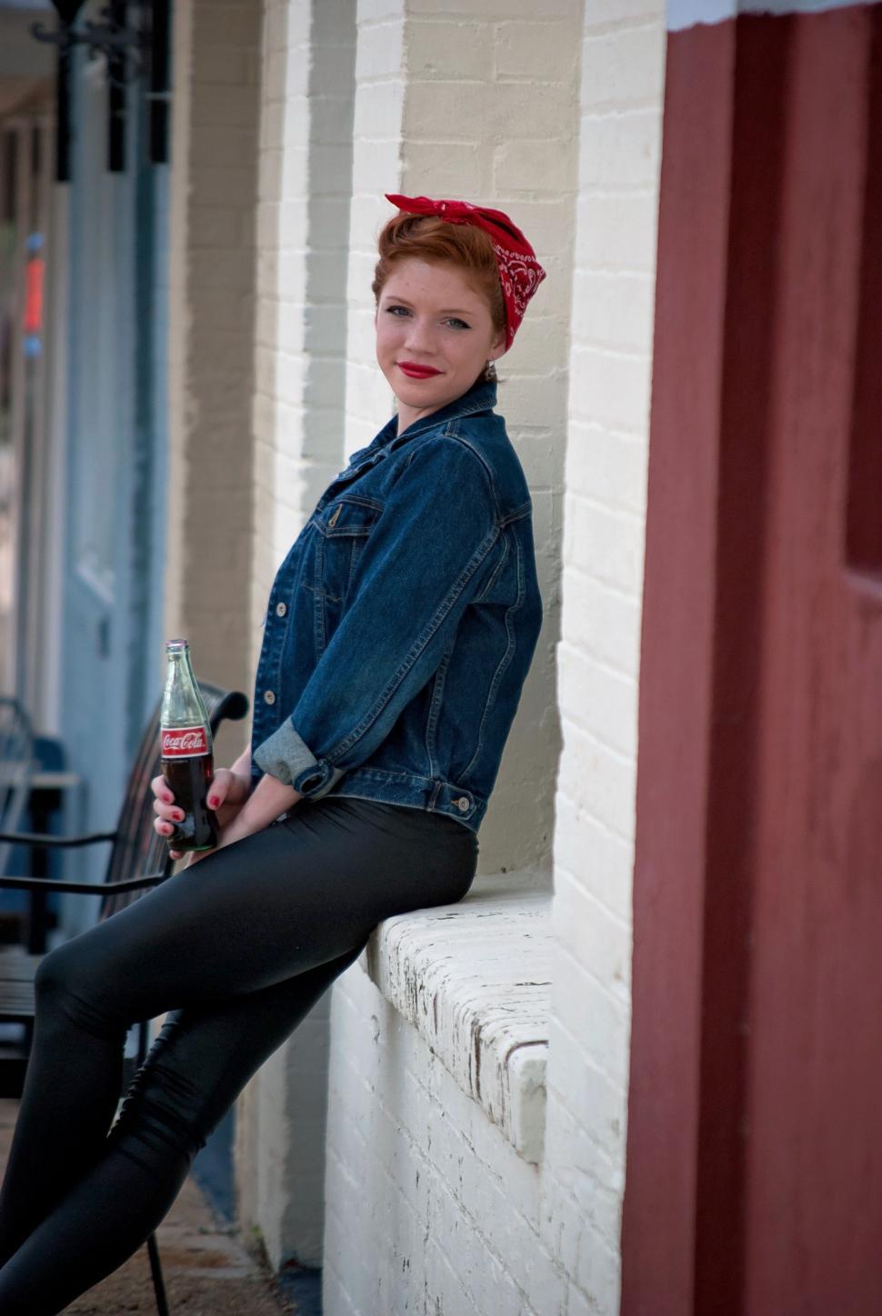 Free Image of Redhead Woman in Vintage Clothing With Coke Bottle Sitting on Window sill 