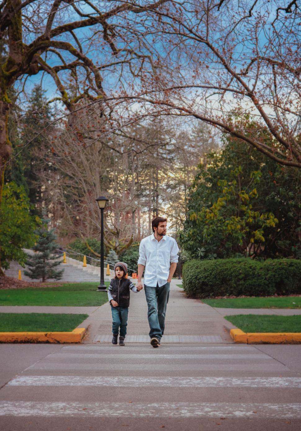 Free Image of Father and Son crossing a road with trees in the background  