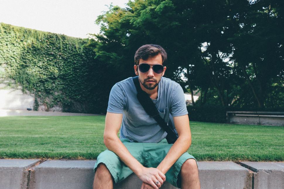 Free Image of Young Man in sunglasses sitting in the park - looking at camera  