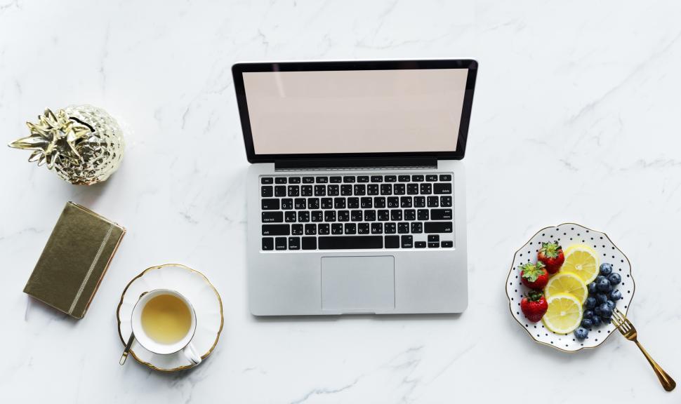Free Image of Overhead view of a laptop on white marble surface with snacks and beverage 