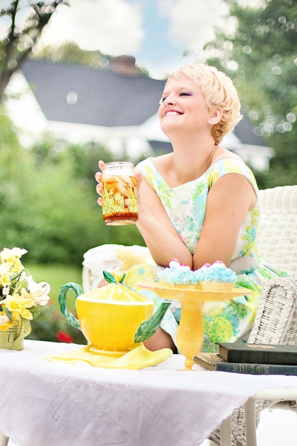 Free Image of Stylish Blonde Woman Laughing and Holding Glass Jar During Breakfast in the garden 