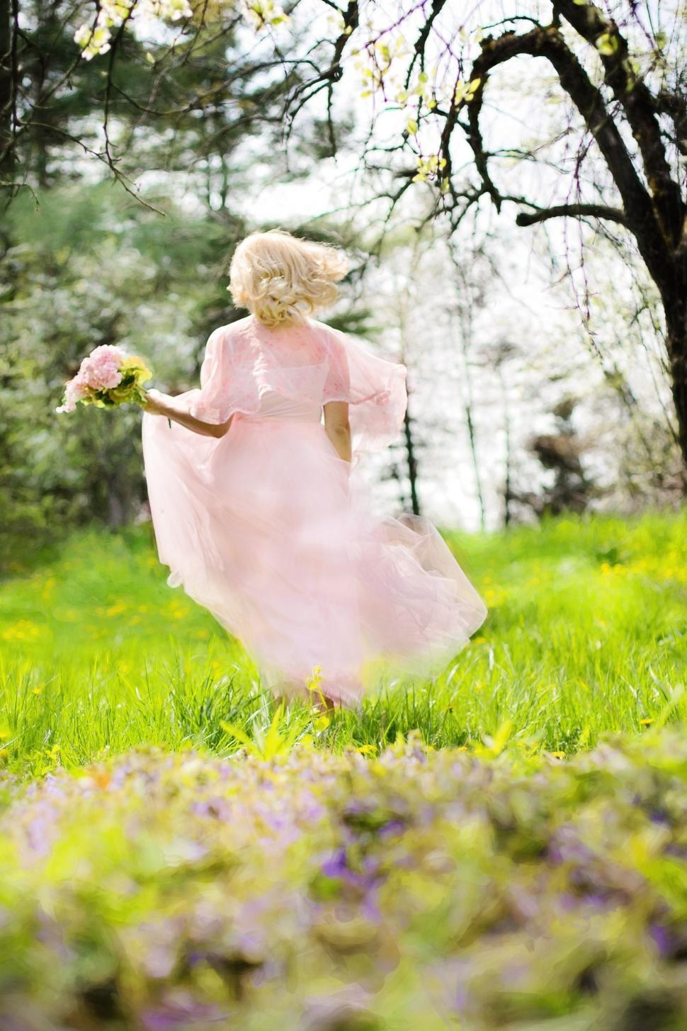 Free Image of Back View of blonde woman holding pink flowers in the meadow 