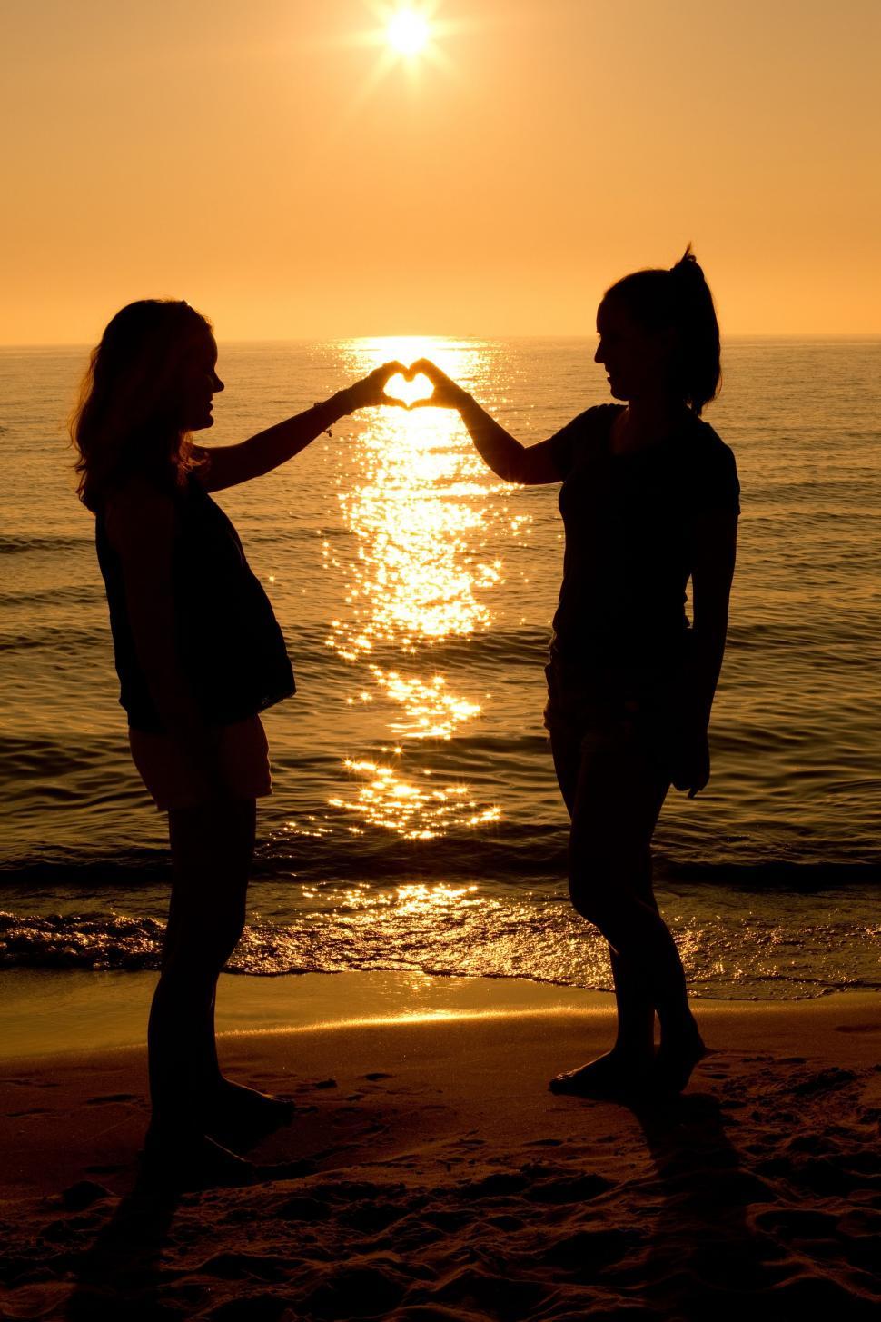 Download Free Stock Photo of Two girls making heart with sunset and ocean 