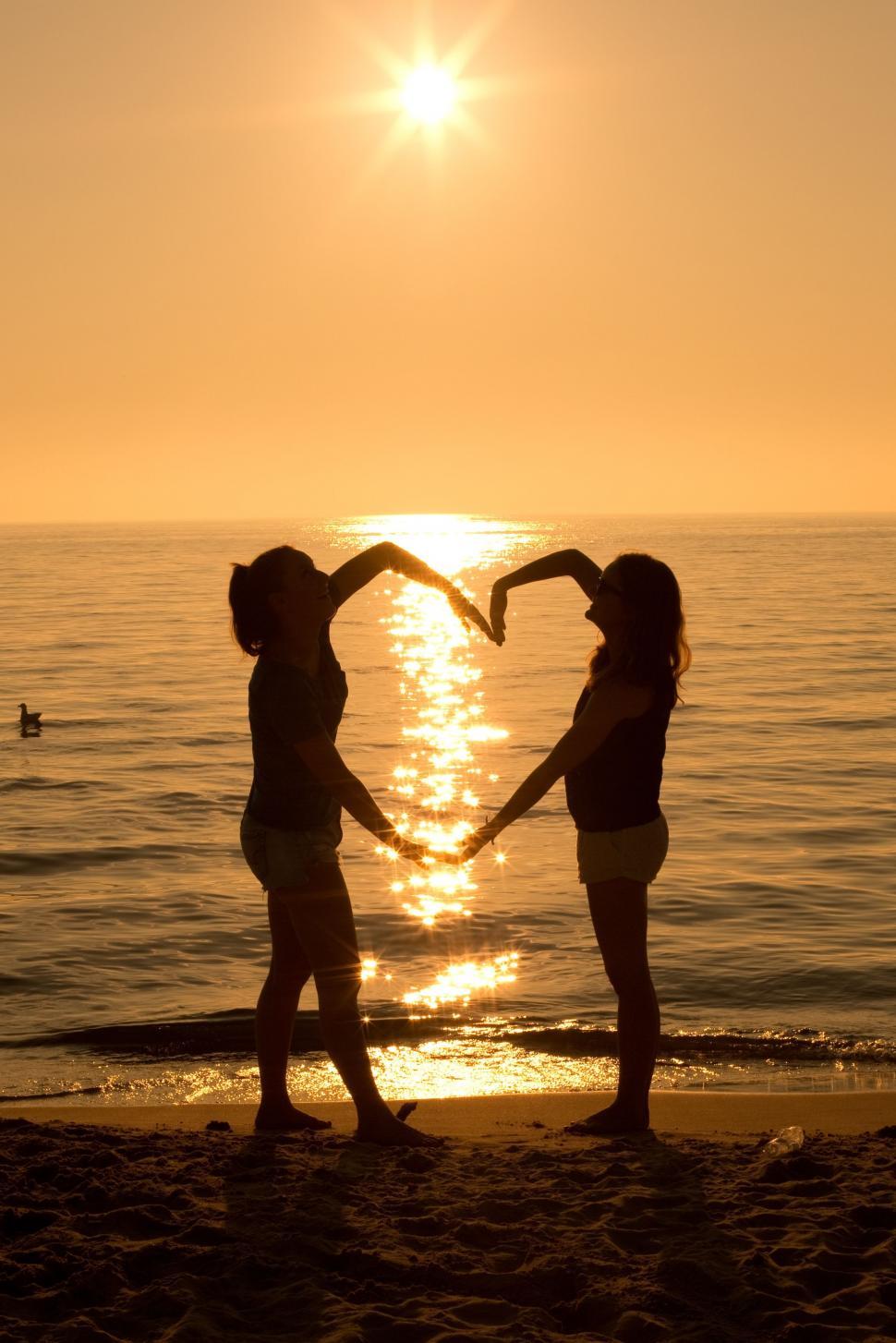 Free Image of Two women making heart with sunset and ocean 