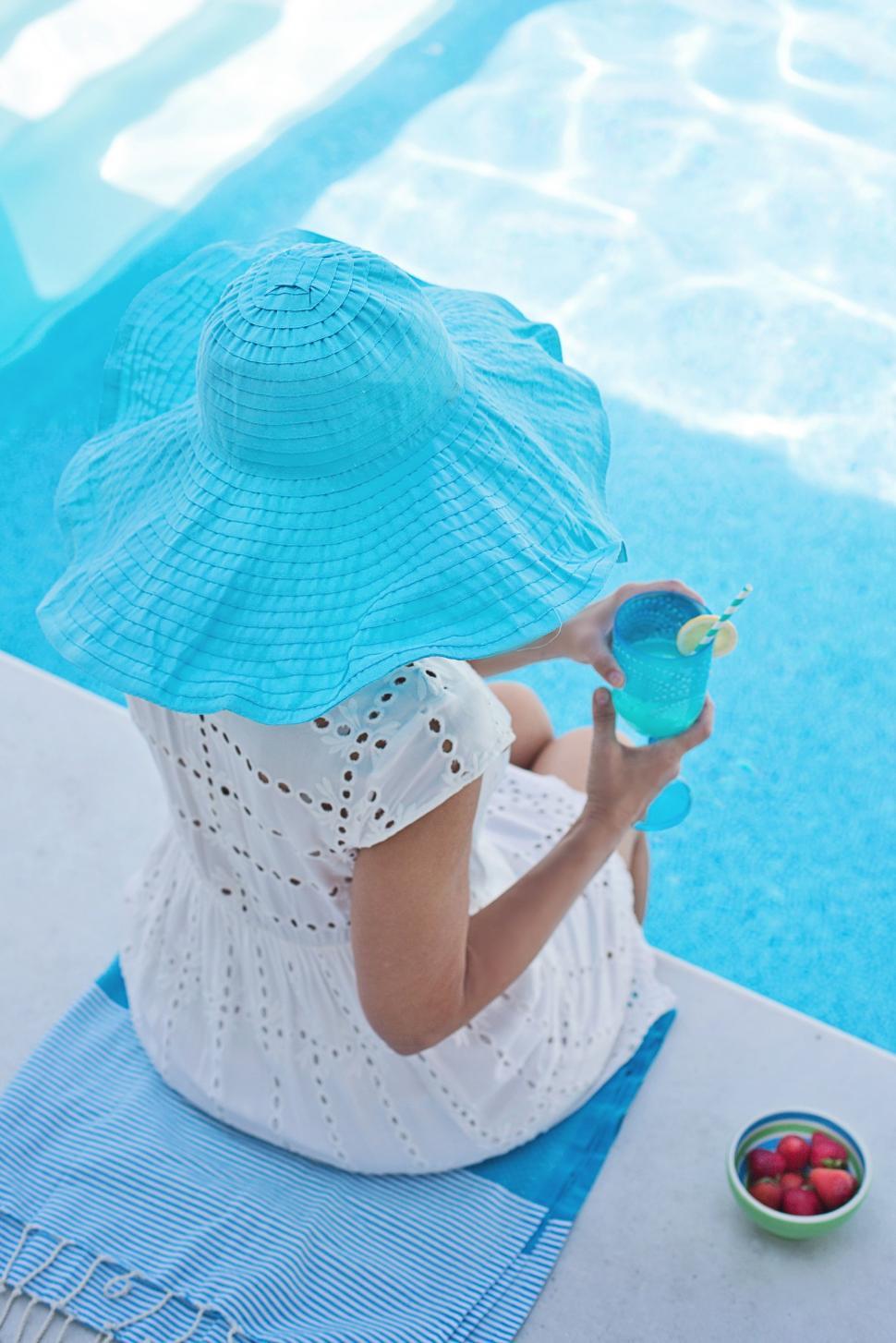 Free Image of Back View of Woman in beach hat with bowl of strawberries at poolside 