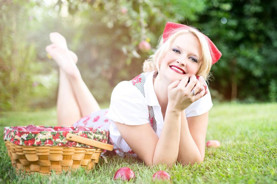 Free Image of Blonde Woman Lying Down on Green Grass With Red Apples 