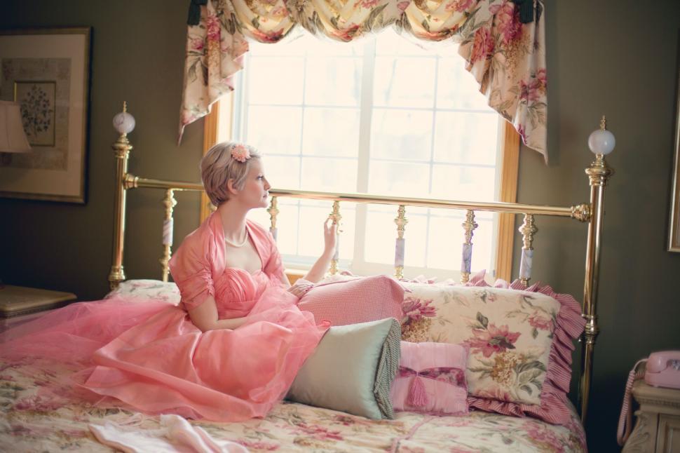 Free Image of Woman on bed with floral print pillows and curtains  