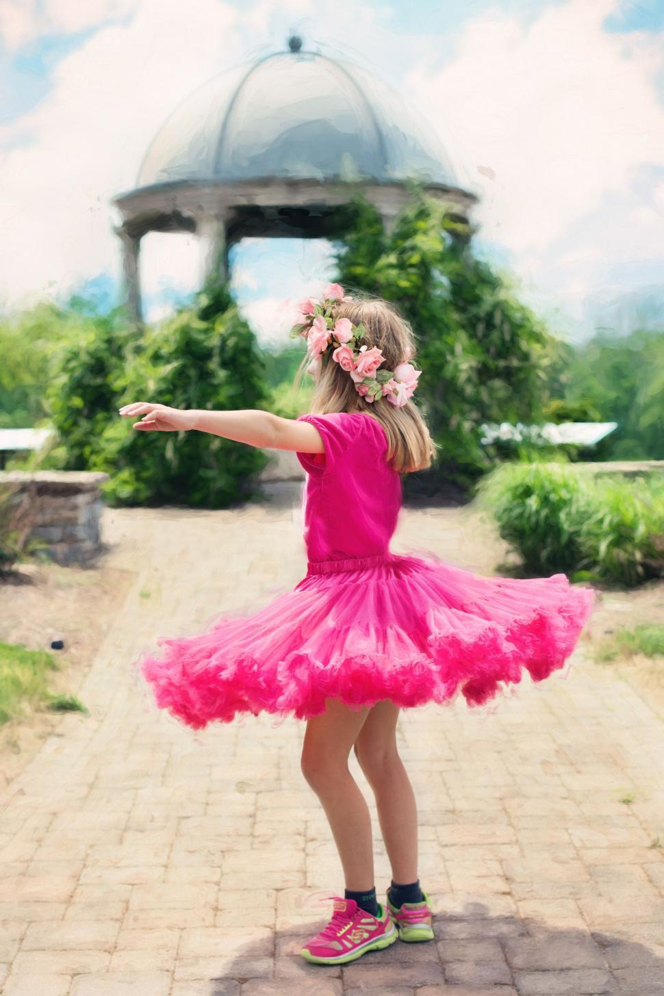 Free Image of Little Girl in pink dress dancing on walking path in the park 