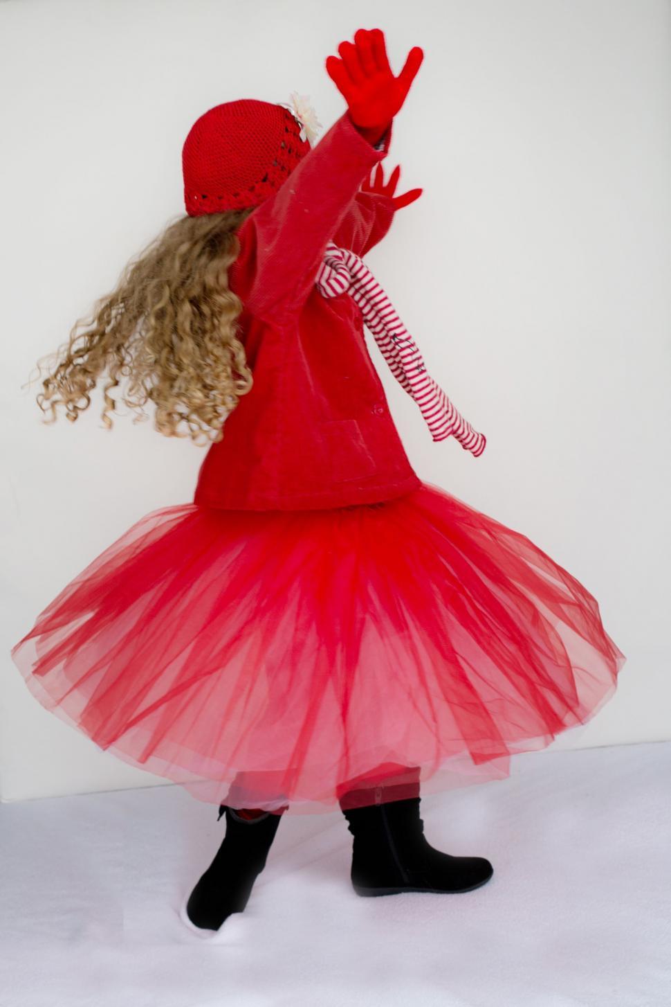 Free Image of Little girl in knitted red cap with red gloves dancing on white background 