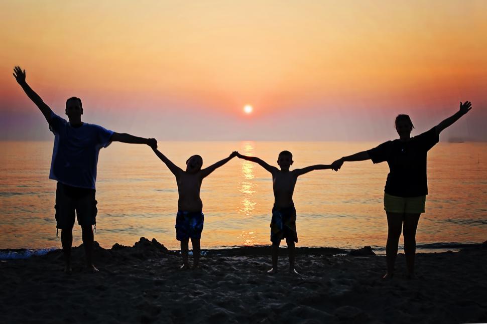Free Image of Happy family holding hands with ocean and sunset in the background 