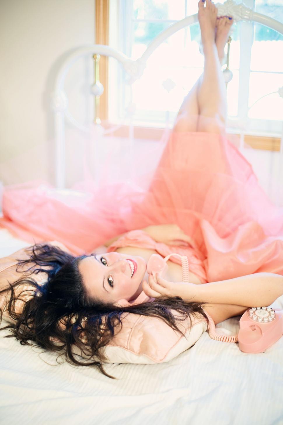 Free Image of Woman With Old Pink Telephone on bed - Looking at camera 