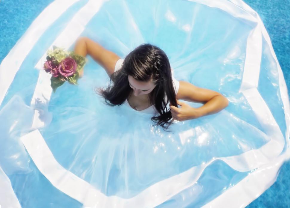 Free Image of Bride standing in pool water with flowers 