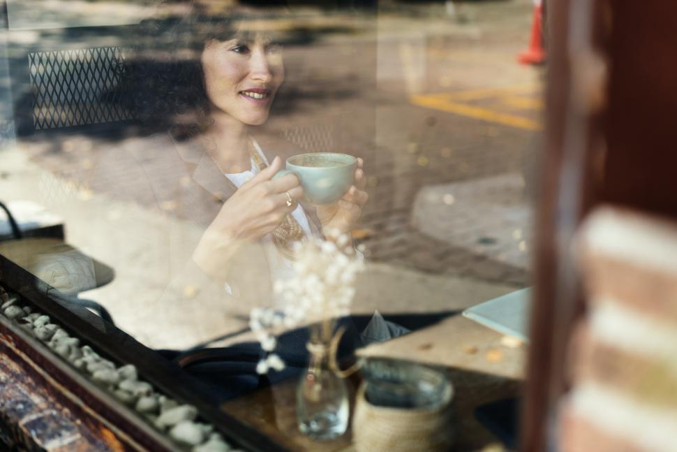 Free Image of Through a reflective window at a woman at a cafe table 