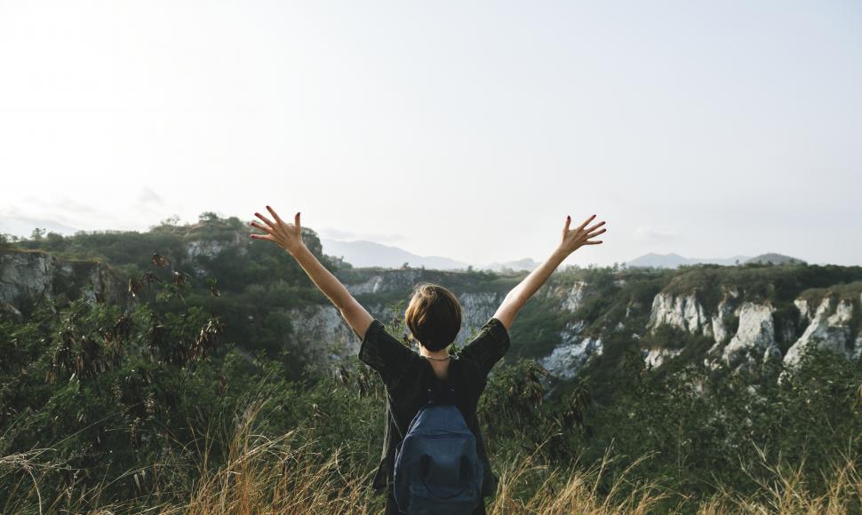 Free Image of View of landscape from behind a young hiker with her hands raised 