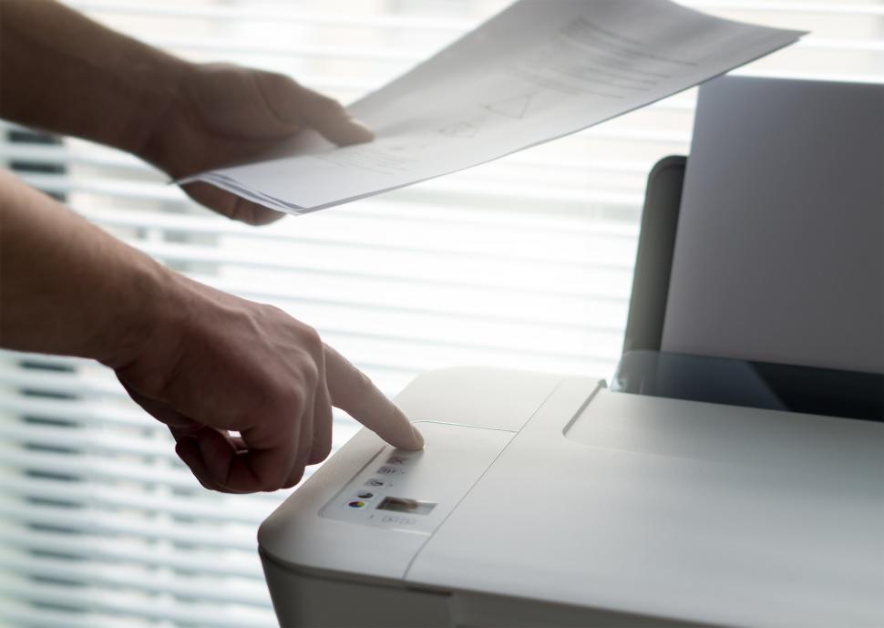 Free Image of Hands holding printed papers over a printer 